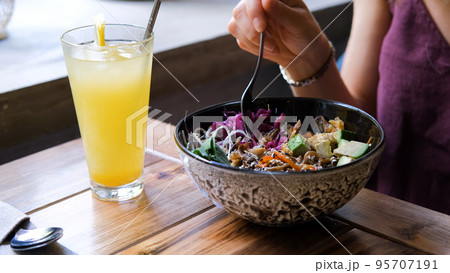 Closeup of young woman eating organic vegan poke bowl with fresh vegetables at restaurant or cafe. Healthy lifestyle and natural organic vegetarian food concept 95707191