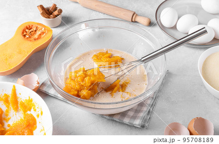 Bowl with pumpkin pie filling and whisk with ingredients for baking a pie on a gray table in the kitchen 95708189