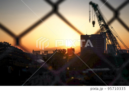 フェンス越しに観る鮮やかな夕陽 95710335