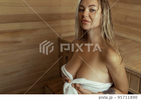 A young woman relaxes and sweats in a hot sauna wrapped in a towel. girl in the sauna. Finnish sauna interior, classic wooden sauna with hot steam. Russian bath. 95711890