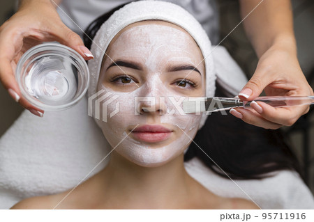 Close-up shot of a woman getting facial treatment with clay mask. Cosmetology and spa 95711916