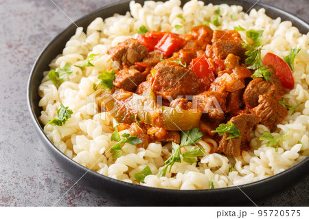 Porkolt is Hungarian for beef stew made by braising meat and simmering it with onions, paprika in a tomato based sauce served with Egg Noodles Nokedli closeup on the plate. Horizontal Porkolt is Hungarian for beef stew made by braising meat and simmering it with onions, paprika in a tomato based sauce served with Egg Noodles Nokedli closeup on the plate. Horizontal 95720575
