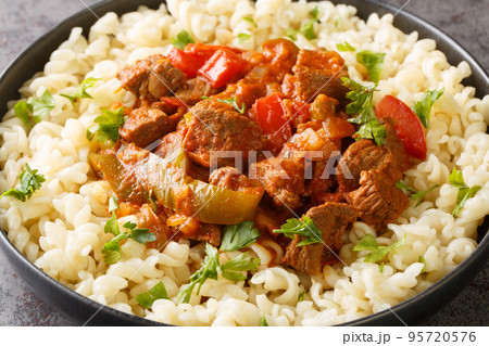 Porkolt is a Hungarian stew with boneless meat, paprika and some vegetables served with Egg Noodles Nokedli closeup on the plate. Horizontal 95720576