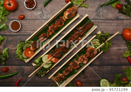 Tasty grilled meat with Sichuan pepper in bamboo barrel plate surrounded by vegetable on rustic wooden table Tasty grilled meat with Sichuan pepper in bamboo barrel plate surrounded by vegetable on rustic wooden table 95721299