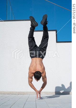 Man doing a handstand outdoors against a white wall. Man doing a handstand outdoors against a white wall. 95721575