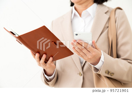 手帳とスマホを持つスーツ姿のミドル女性 手帳とスマホを持つスーツ姿のミドル女性 95721901