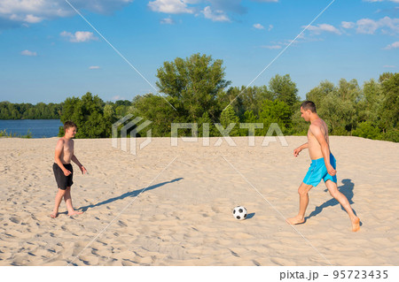The concept of sports and active games in the summer. Father and son play with a ball on the beach. Beach soccer, vacation, lifestyle The concept of sports and active games in the summer. Father and son play with a ball on the beach. Beach soccer, vacation, lifestyle 95723435