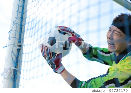 サッカーボールをキャッチするゴールキーパーの男性 95725179