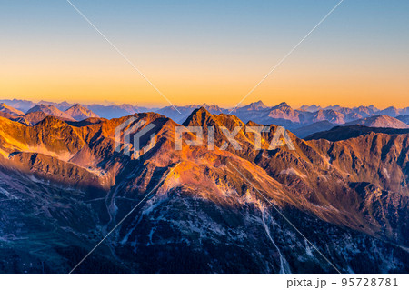 Alpine mountain peaks illuminated by rising sun Alpine mountain peaks illuminated by rising sun 95728781