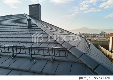 Closeup snow guard for safety in winter on house roof top covered with ceramic shingles. Tiled covering of building Closeup snow guard for safety in winter on house roof top covered with ceramic shingles. Tiled covering of building 95731426