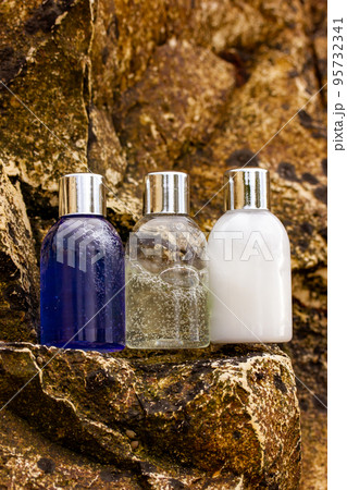 Plastic bottles with natural cosmetic in travel containers - shower gel, shampoo with bubbles inside, body lotion in miniature containers against a rock background. Face body care vertical photo. Plastic bottles with natural cosmetic in travel containers - shower gel, shampoo with bubbles inside, body lotion in miniature containers against a rock background. Face body care vertical photo. 95732341