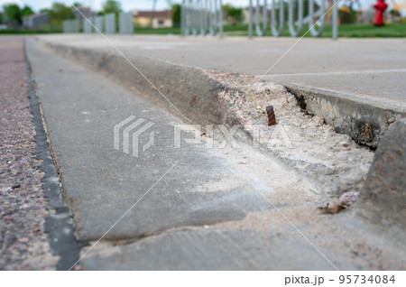 Broken sidewalk curb with exposed rebar and jagged edges that could cause a tripping hazard Broken sidewalk curb with exposed rebar and jagged edges that could cause a tripping hazard 95734084