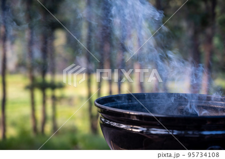 Focus on a portable charcoal grill at a campsite overlooking a green forest Focus on a portable charcoal grill at a campsite overlooking a green forest 95734108