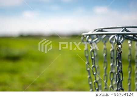 Disc golf goal chains gently swaying in the breeze with a green course in the background Disc golf goal chains gently swaying in the breeze with a green course in the background 95734124
