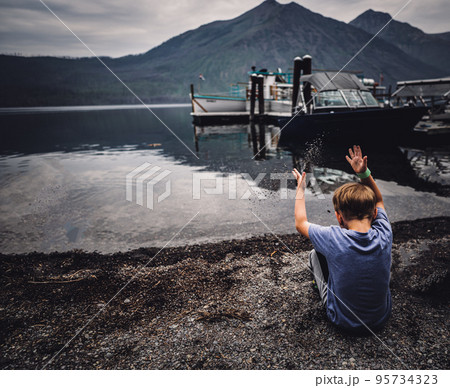 Young boy tossing sand into Lake McDonald at Glacier National Park 95734323
