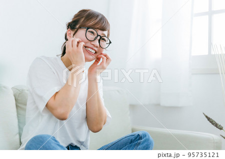 ソファに座りながら照れて爆笑するメガネをかけたアジア人女性 ソファに座りながら照れて爆笑するメガネをかけたアジア人女性 95735121