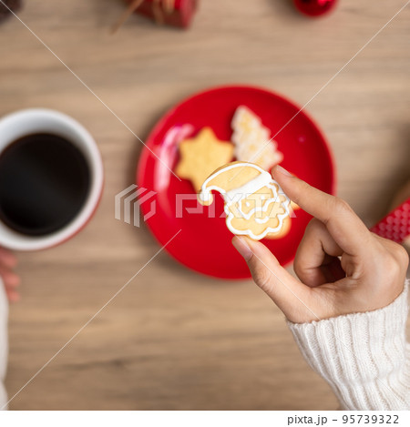 Merry Christmas with woman hand holding coffee cup and homemade cookie on table. Xmas eve, party, holiday and happy New Year concept 95739322
