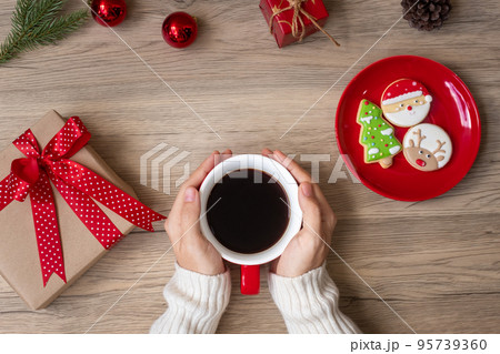 Merry Christmas with woman hand holding coffee cup and homemade cookie on table. Xmas eve, party, holiday and happy New Year concept Merry Christmas with woman hand holding coffee cup and homemade cookie on table. Xmas eve, party, holiday and happy New Year concept 95739360