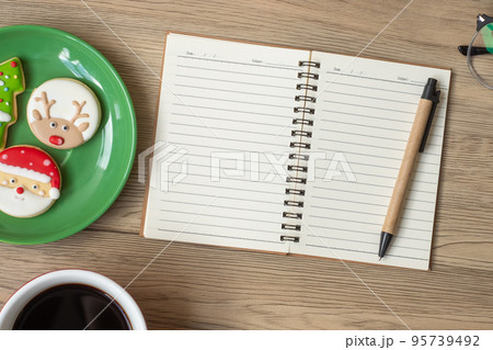 Blank notebook, black coffee cup, Christmas cookies and pen on wood table, Top view and copy space. Xmas, Happy New Year, Goals, Resolution, To do list, Strategy and Plan concept 95739492