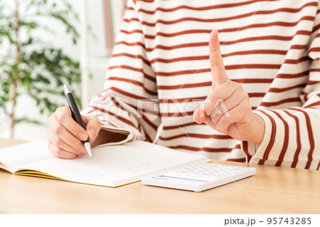 家計簿をつけながら人差し指を立てるカジュアル姿のミドル女性 95743285