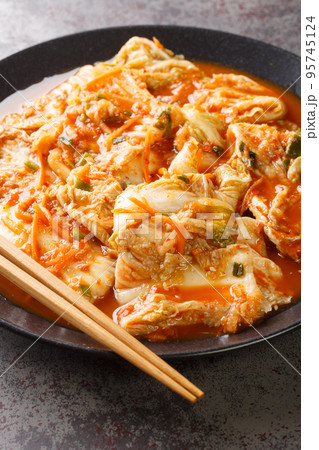 Eating kimchi cabbage in a bowl with chopsticks, Korean food close-up in a black dish. Vertical Eating kimchi cabbage in a bowl with chopsticks, Korean food close-up in a black dish. Vertical 95745124