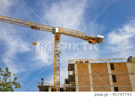 Construction tower crane on the construction site of a modern brick residential building, against the background of sunlight, sunrise, summer 95747743