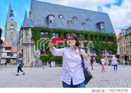 Woman tourist taking selfie in an old european city, in front of historical building Woman tourist taking selfie in an old european city, in front of historical building 95754570