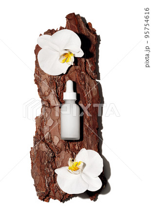 White glass cosmetic bottle on textured tree bark podium with white orchid flowers in rays of sunlight with hard shadows. Demonstration of cosmetic product with copy space in flat lay style. 95754616