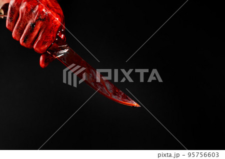 A man with bloody hands brandishes a knife on a black background.  95756603