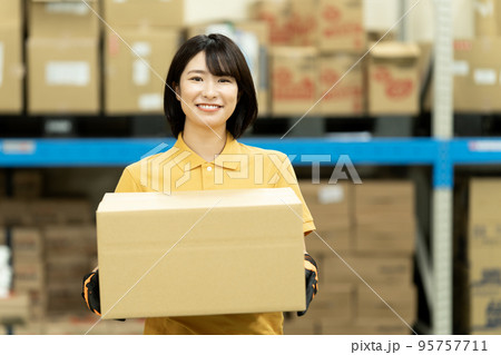 倉庫でダンボールを運ぶ女性スタッフ 95757711