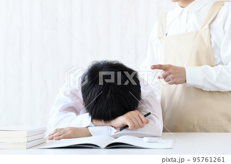 机に頭を伏せる子供と叱る母親 95761261