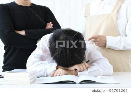 机に頭を伏せる子供と叱る母親と父親 95761262