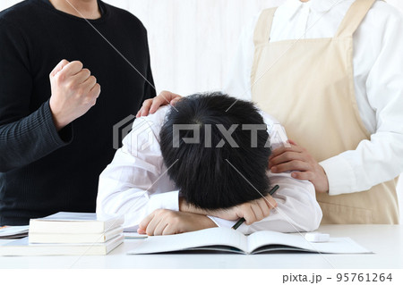 机に頭を伏せる子供と励ます母親と父親 95761264