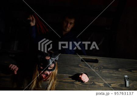 nipple tapes. A woman is imprisoned in a wooden pillory during sexual games. BDSM Erotic fantasies. Subordination. Toys for adults. The mask of the cat. The man in the shirt dominates. 95763137
