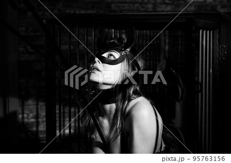 BDSM A woman in a leather cat mask on a leash in an iron cage obeys her lover. Role-playing games for adults. The man dominates and punishes the mistress. Monochrome photo. BDSM A woman in a leather cat mask on a leash in an iron cage obeys her lover. Role-playing games for adults. The man dominates and punishes the mistress. Monochrome photo. 95763156