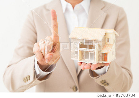 戸建て住宅の模型を持って人差し指を立てるスーツ姿のミドル女性 戸建て住宅の模型を持って人差し指を立てるスーツ姿のミドル女性 95763734