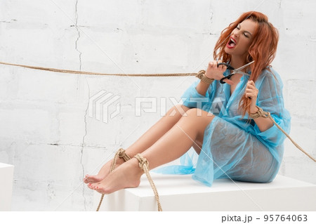 Mad alluring lady with bound hands and legs shouting and cutting hair 95764063