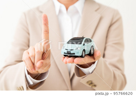 車の模型を持って人差し指を立てるスーツ姿のミドル女性 95766620