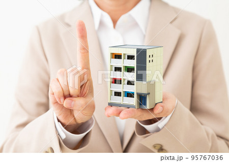 マンションの住宅模型を持って人差し指を立てるスーツ姿のミドル女性 マンションの住宅模型を持って人差し指を立てるスーツ姿のミドル女性 95767036