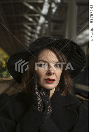 Portrait of middle-aged aristocratic woman in black wide-brimmed hat with veil and lace gloves. Portrait of middle-aged aristocratic woman in black wide-brimmed hat with veil and lace gloves. 95767542