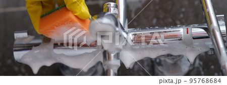 Cleaning lady in rubber glove washes faucet in bathroom with sponge with foam Cleaning lady in rubber glove washes faucet in bathroom with sponge with foam 95768684