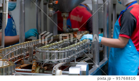 Canned fish factory. Food industry.  Sardines in red tomato sauce in tinned cans on conveyor belt at food factory. Blur workers working in food processing production line. Food manufacturing industry. 95768810