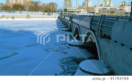 Arched bridge close-up over a frozen river against the backdrop of a city illuminated by the sun Arched bridge close-up over a frozen river against the backdrop of a city illuminated by the sun 95769768