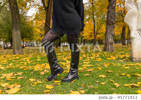 A girl in warm boots poses against a background of fallen foliage A girl in warm boots poses against a background of fallen foliage 95771911