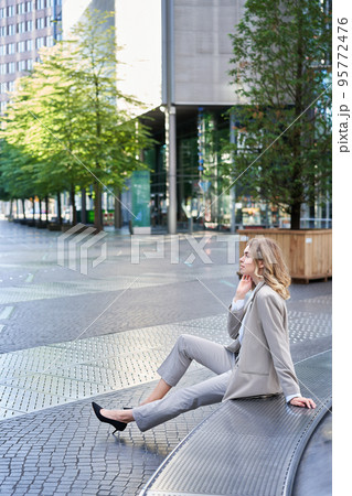 Vertical shot of young business woman in beige suit, office worker taking break outside near office building 95772476