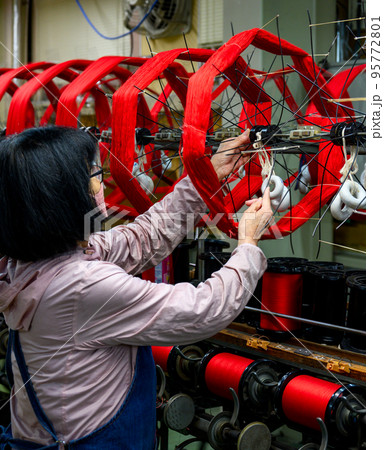 赤く染められた絹糸を巻き取る作業をする女性 95772801