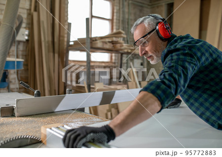 Carpenter in ear protectors working in a workshop 95772883