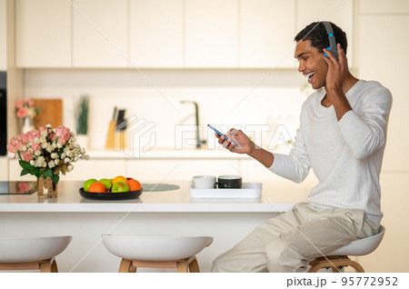 Young man sitting in the kitchen and listening to music in headphones 95772952