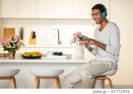 Young man sitting in the kitchen and listening to music in headphones 95772956