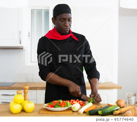 Proffesional male cook in black uniform chopping vegetables Proffesional male cook in black uniform chopping vegetables 95774640